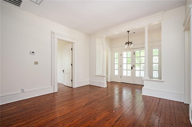 unfurnished living room featuring dark wood-type flooring, a chandelier, and ornate columns