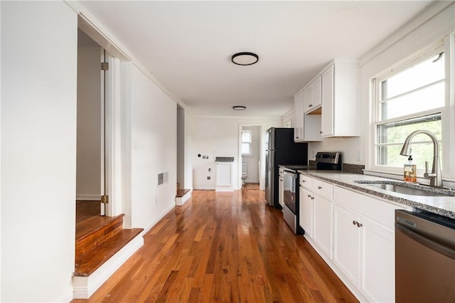 kitchen featuring sink, stainless steel appliances, white cabinets, dark hardwood / wood-style flooring, and dark stone counters