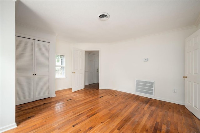 unfurnished bedroom featuring hardwood / wood-style floors, ornamental molding, and a closet