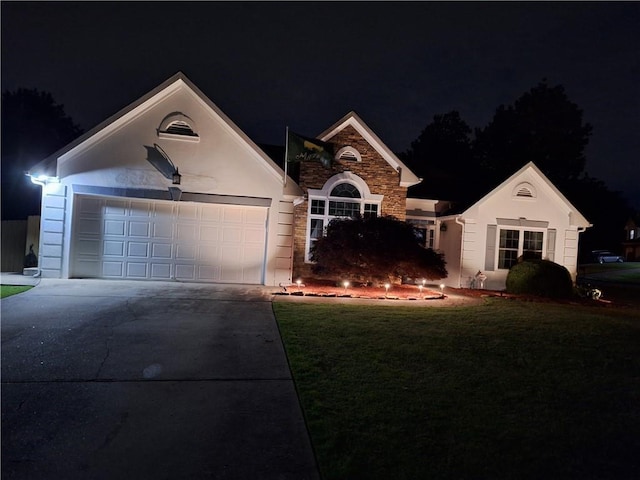 view of front facade with a yard, a garage, concrete driveway, stone siding, and stucco siding