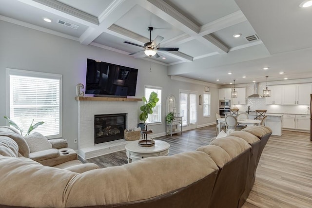 living room with beam ceiling, crown molding, a brick fireplace, and light wood-type flooring