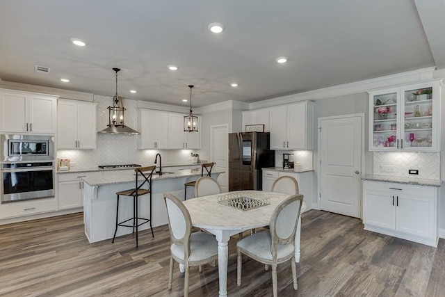 kitchen with decorative light fixtures, a center island with sink, stainless steel appliances, light stone countertops, and white cabinets