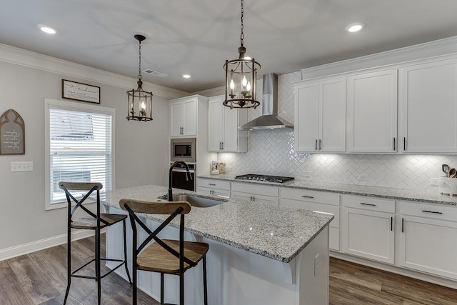 kitchen with appliances with stainless steel finishes, white cabinetry, an island with sink, a kitchen bar, and wall chimney exhaust hood