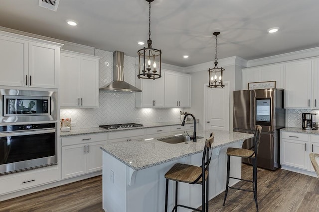 kitchen with wall chimney exhaust hood, sink, an island with sink, stainless steel appliances, and white cabinets