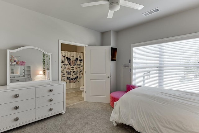 bedroom featuring ceiling fan, light colored carpet, and ensuite bath