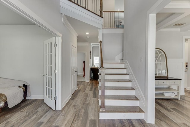 staircase featuring a towering ceiling, ornamental molding, and hardwood / wood-style floors