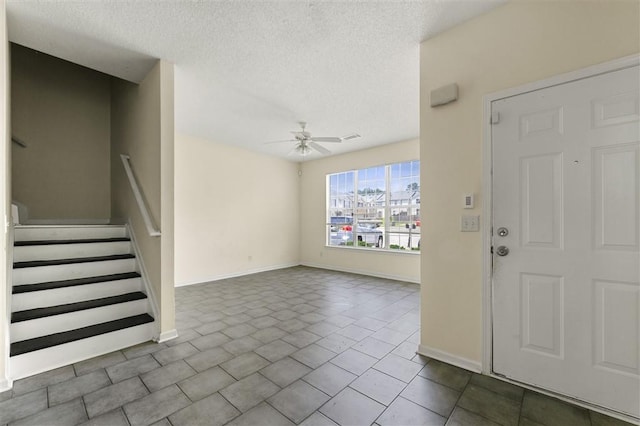entrance foyer with a ceiling fan, baseboards, a textured ceiling, stairs, and tile patterned floors