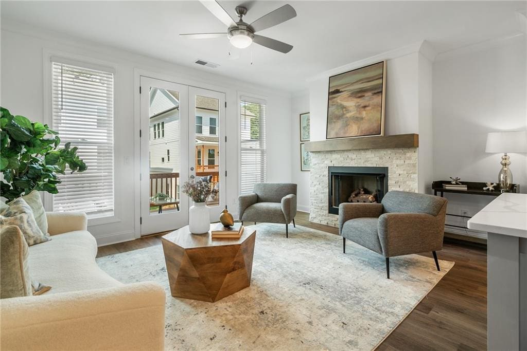 sitting room featuring a stone fireplace, ceiling fan, dark hardwood / wood-style flooring, and crown molding