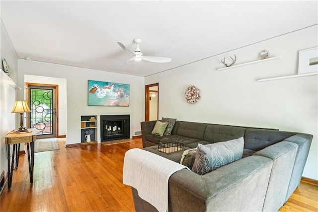living room featuring wood-type flooring, a ceiling fan, a fireplace with flush hearth, and baseboards