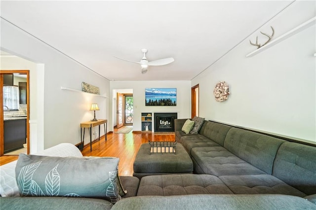 living area featuring light wood-type flooring, a ceiling fan, and a fireplace