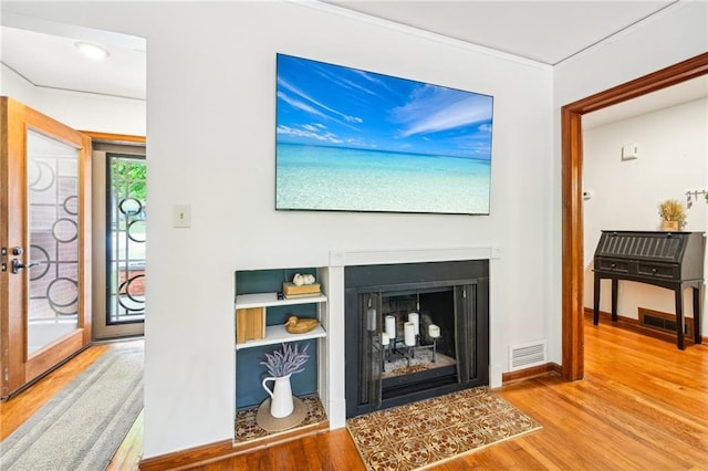 living area featuring wood finished floors, a fireplace with raised hearth, ornamental molding, and baseboards