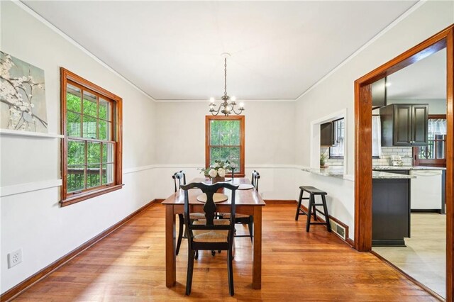 dining space with ornamental molding, a chandelier, light wood finished floors, and baseboards