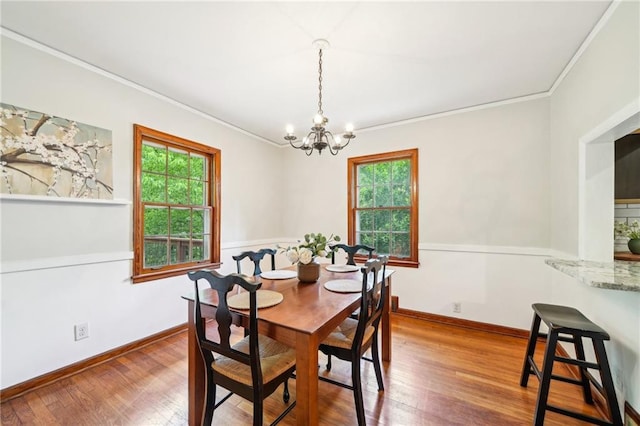 dining area featuring a chandelier, healthy amount of natural light, ornamental molding, wood finished floors, and baseboards