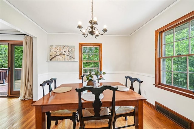 dining space with a chandelier, healthy amount of natural light, ornamental molding, and a wainscoted wall