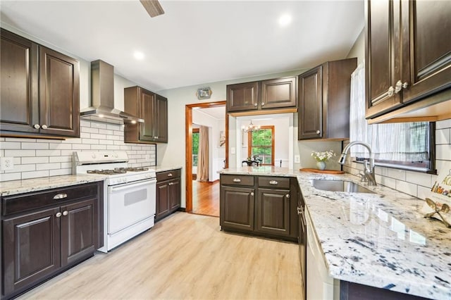 kitchen featuring white gas stove, wall chimney exhaust hood, a sink, light wood-type flooring, and dark brown cabinetry