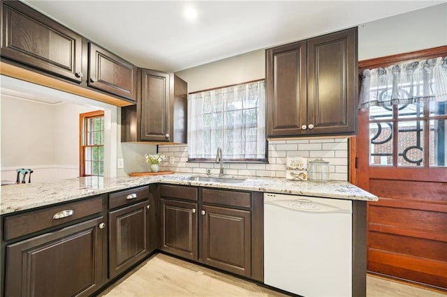 kitchen with white dishwasher, a sink, dark brown cabinets, decorative backsplash, and light stone countertops
