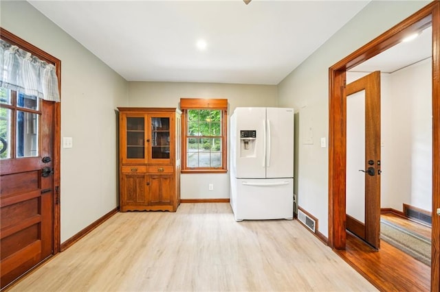 kitchen featuring white fridge with ice dispenser, light wood finished floors, and baseboards