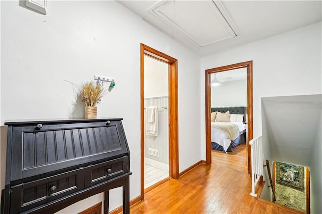 hall featuring attic access, wood finished floors, and baseboards