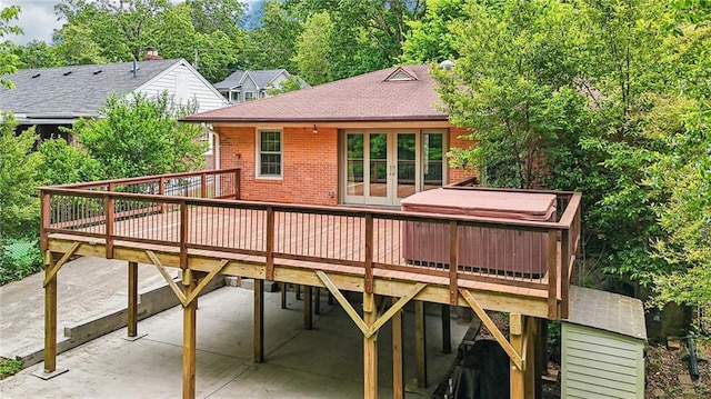 rear view of property with brick siding, a wooden deck, a patio, a shingled roof, and french doors