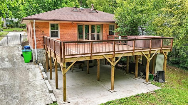 rear view of property featuring a deck, brick siding, roof with shingles, fence, and a carport