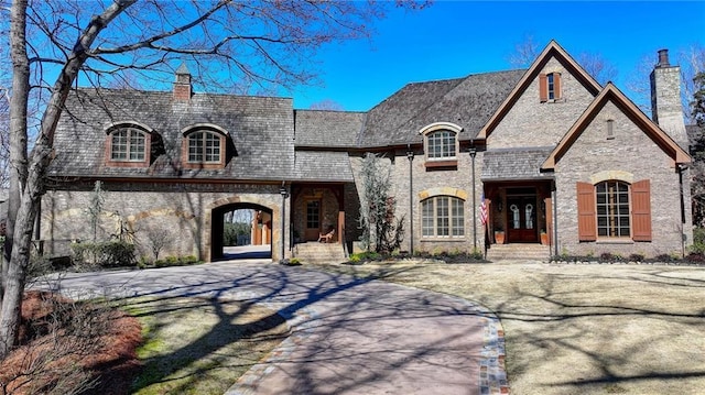 french country style house featuring brick siding, concrete driveway, and a chimney