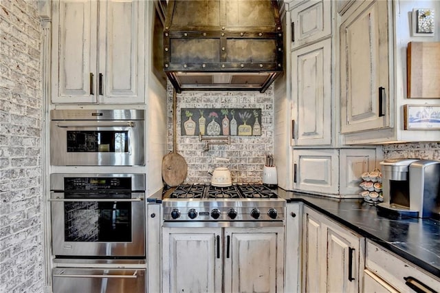 kitchen with brick wall, appliances with stainless steel finishes, dark countertops, a warming drawer, and tasteful backsplash