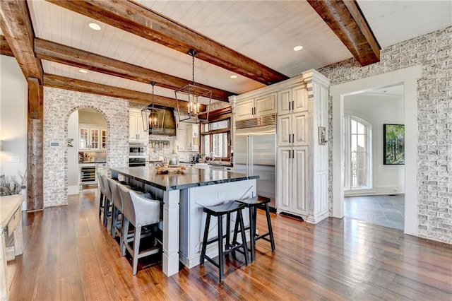 kitchen featuring beamed ceiling, a breakfast bar, stainless steel built in fridge, dark wood-style floors, and arched walkways