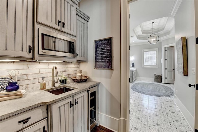 kitchen with stainless steel microwave, backsplash, a tray ceiling, ornamental molding, and a sink