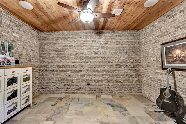 interior space featuring stone finish flooring, wood ceiling, brick wall, and a ceiling fan