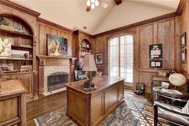 office featuring built in features, wood walls, a fireplace, ceiling fan, and dark wood-style flooring