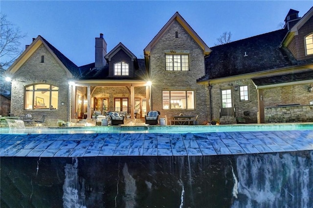 rear view of property with brick siding, a swimming pool, a chimney, outdoor lounge area, and a patio area