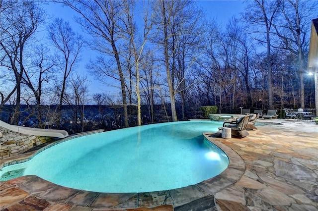 view of swimming pool featuring a pool with connected hot tub, a water slide, and a patio area