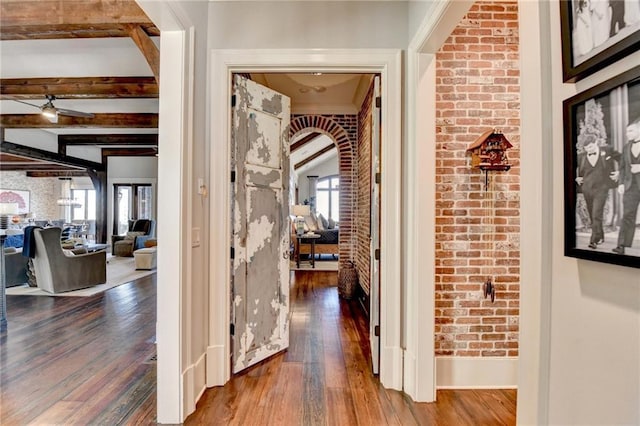 hall featuring arched walkways, beam ceiling, and brick wall