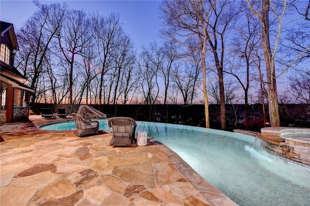 pool at dusk featuring a fenced in pool, an in ground hot tub, a water slide, and a fenced backyard