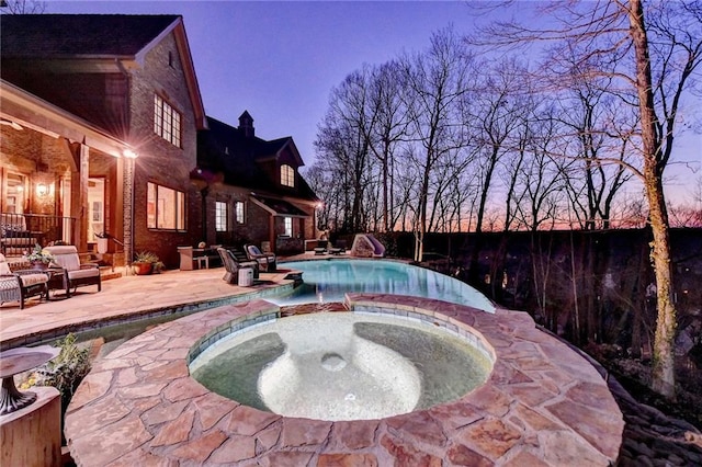 pool at dusk featuring a patio area, an outdoor pool, an in ground hot tub, and a water slide