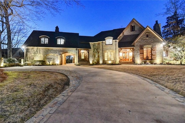 french country style house featuring stone siding, curved driveway, and a chimney