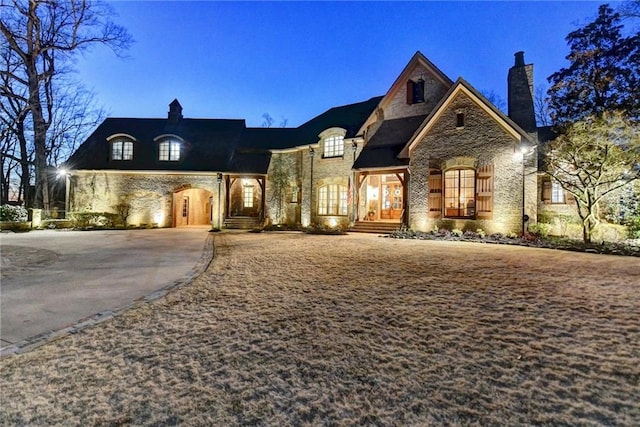 french country style house with stone siding, driveway, and a chimney