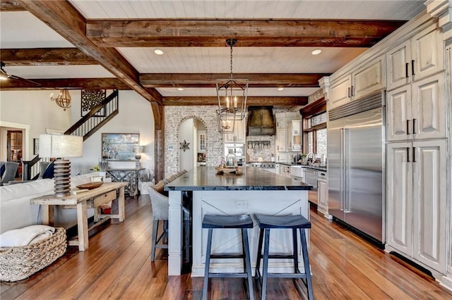 kitchen with built in refrigerator, a breakfast bar, dark countertops, open floor plan, and arched walkways