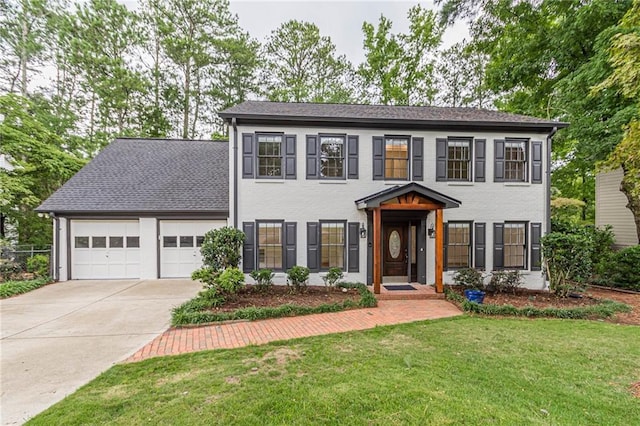 colonial home featuring driveway, a shingled roof, an attached garage, a front lawn, and brick siding