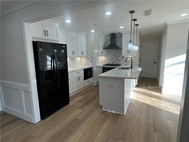 kitchen featuring a sink, black fridge with ice dispenser, visible vents, wall chimney exhaust hood, and light wood finished floors