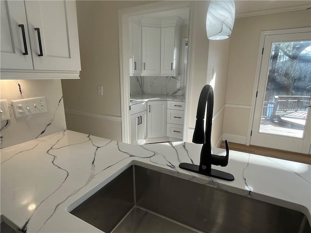 kitchen with light stone counters, white cabinets, a sink, and crown molding