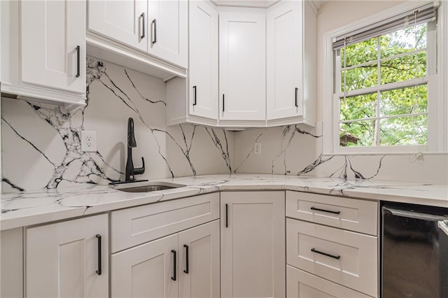 kitchen with light stone countertops, backsplash, white cabinets, and a sink