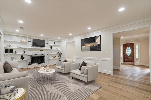 living room with light wood-style floors, visible vents, a fireplace with raised hearth, and crown molding