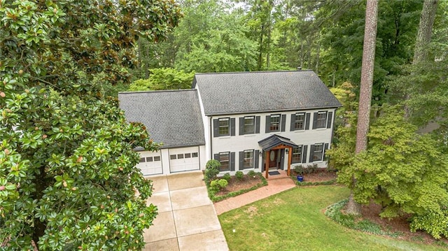 colonial-style house featuring concrete driveway, a front lawn, roof with shingles, and an attached garage