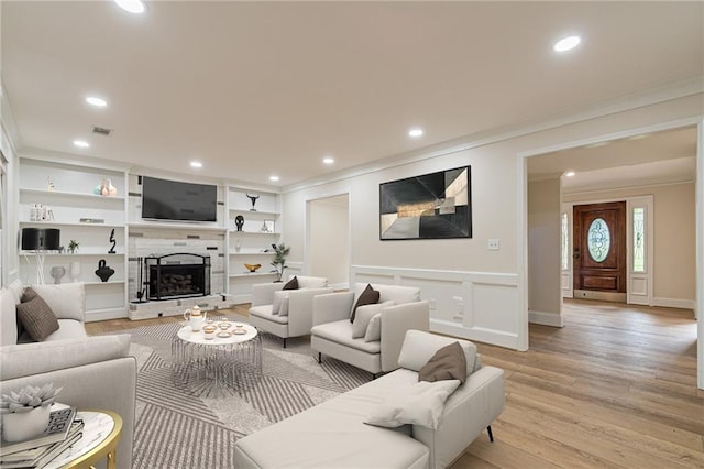 living area featuring a tile fireplace, visible vents, built in features, light wood-style floors, and crown molding