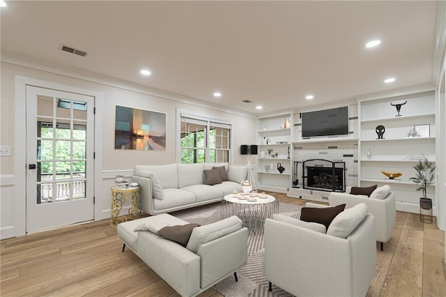 living room with light wood finished floors, visible vents, a tiled fireplace, crown molding, and recessed lighting