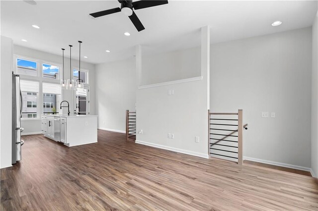 unfurnished living room featuring ceiling fan with notable chandelier, wood-type flooring, and sink