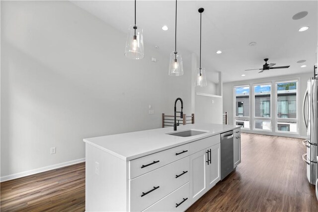 kitchen with stainless steel appliances, sink, white cabinets, hanging light fixtures, and an island with sink