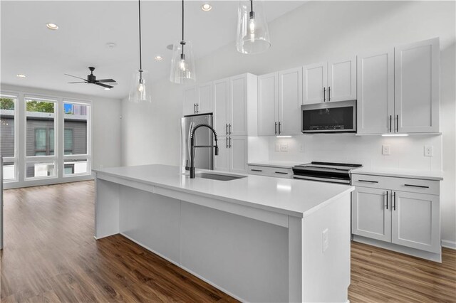 kitchen featuring electric range oven, a kitchen island with sink, sink, white cabinetry, and hanging light fixtures