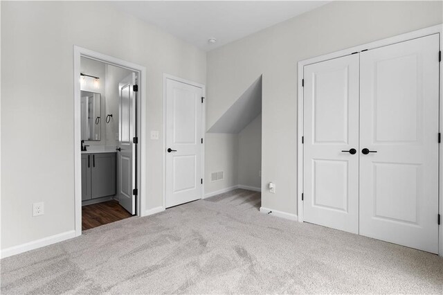 unfurnished bedroom featuring a closet, light carpet, and ensuite bath